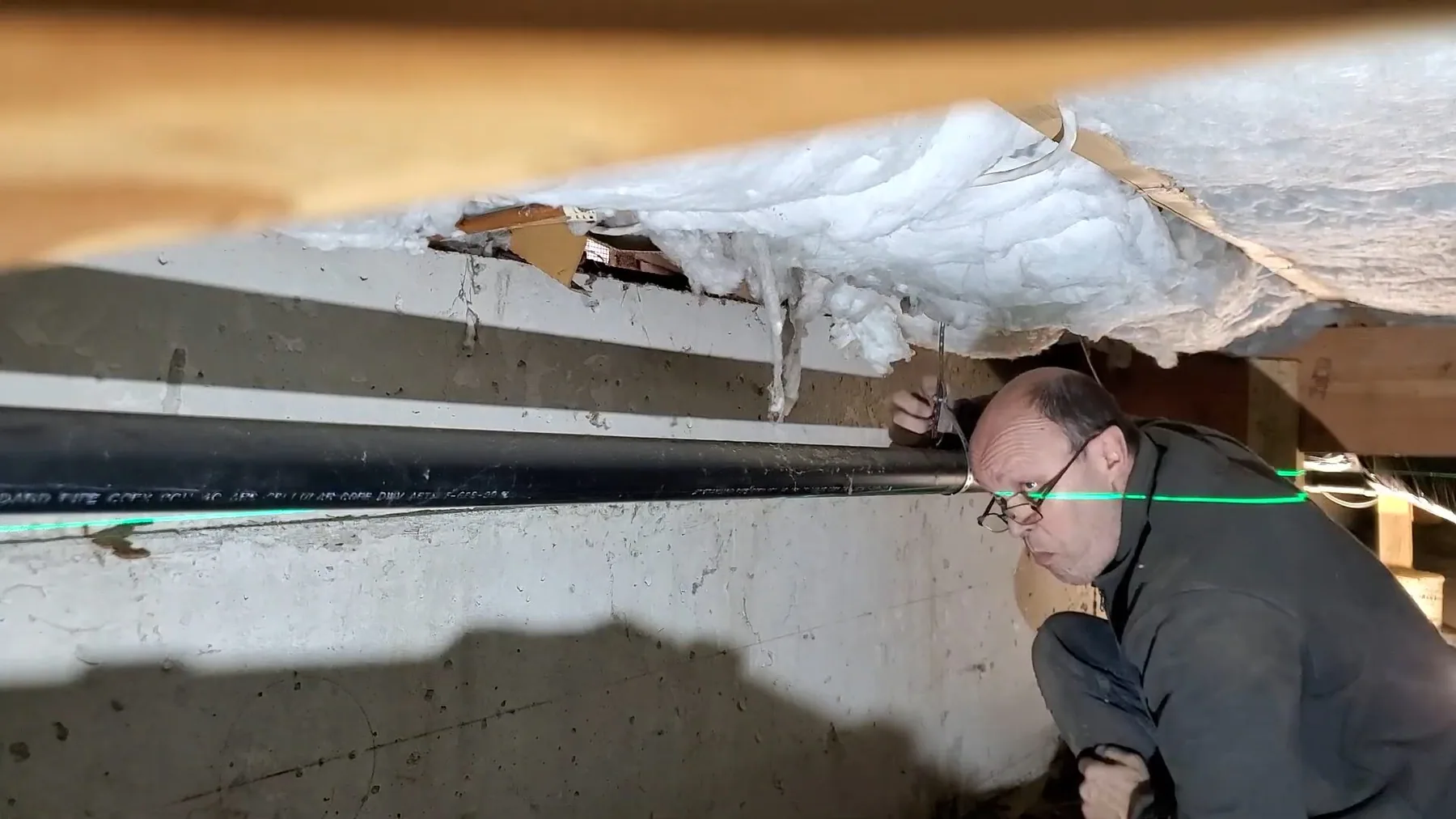 Worker inspecting crawlspace pipe from outside, photographed on a local plumbing job